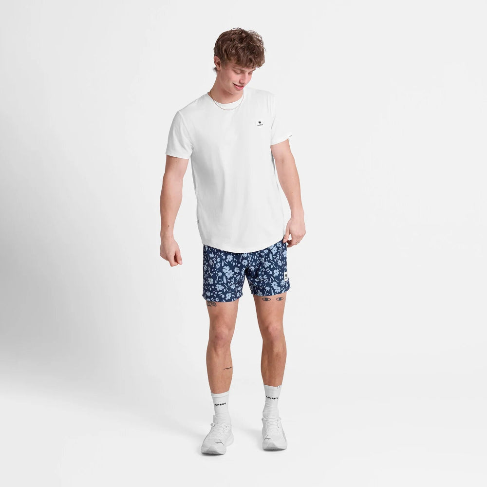 Man wearing a white t-shirt and blue patterned shorts on a light gray background