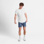 Man wearing a white t-shirt and blue patterned shorts on a light gray background