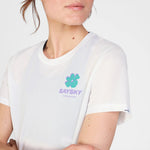 Person wearing a white t-shirt with a logo and text on a plain background