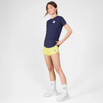 Woman wearing a navy blue t-shirt, yellow shorts, and white sneakers on a white background