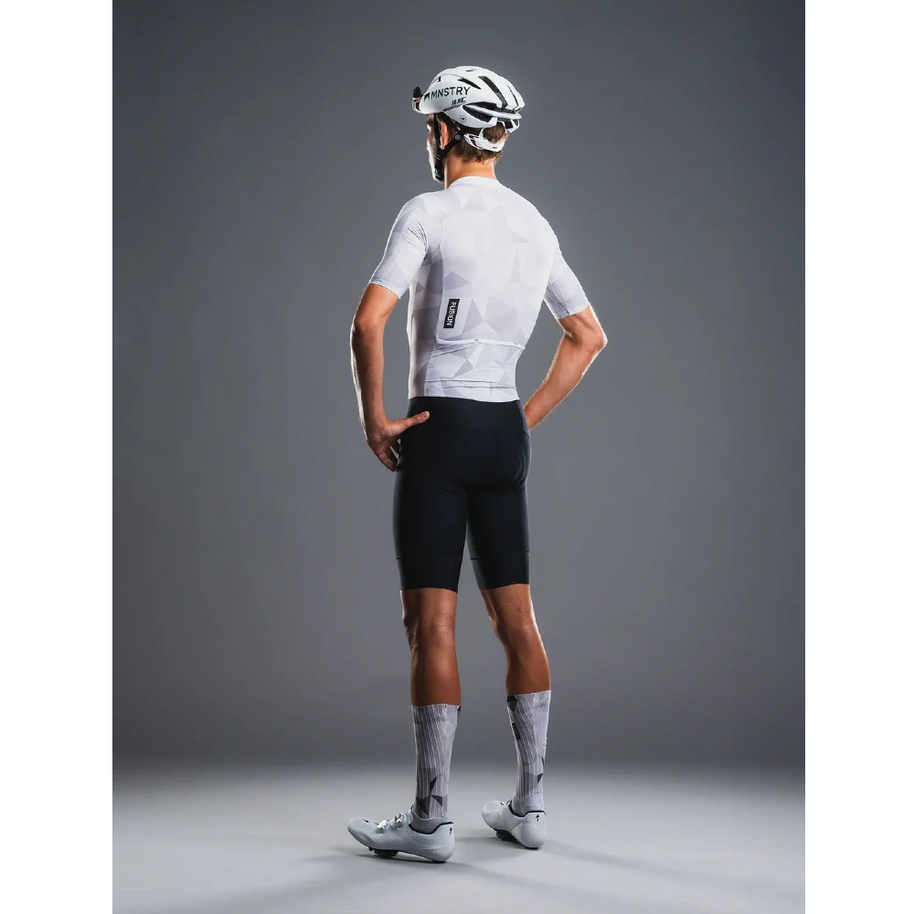 Person wearing a white cycling jersey and black shorts with a helmet on a gray background