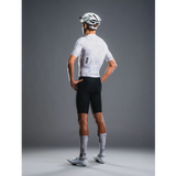 Person wearing a white cycling jersey and black shorts with a helmet on a gray background