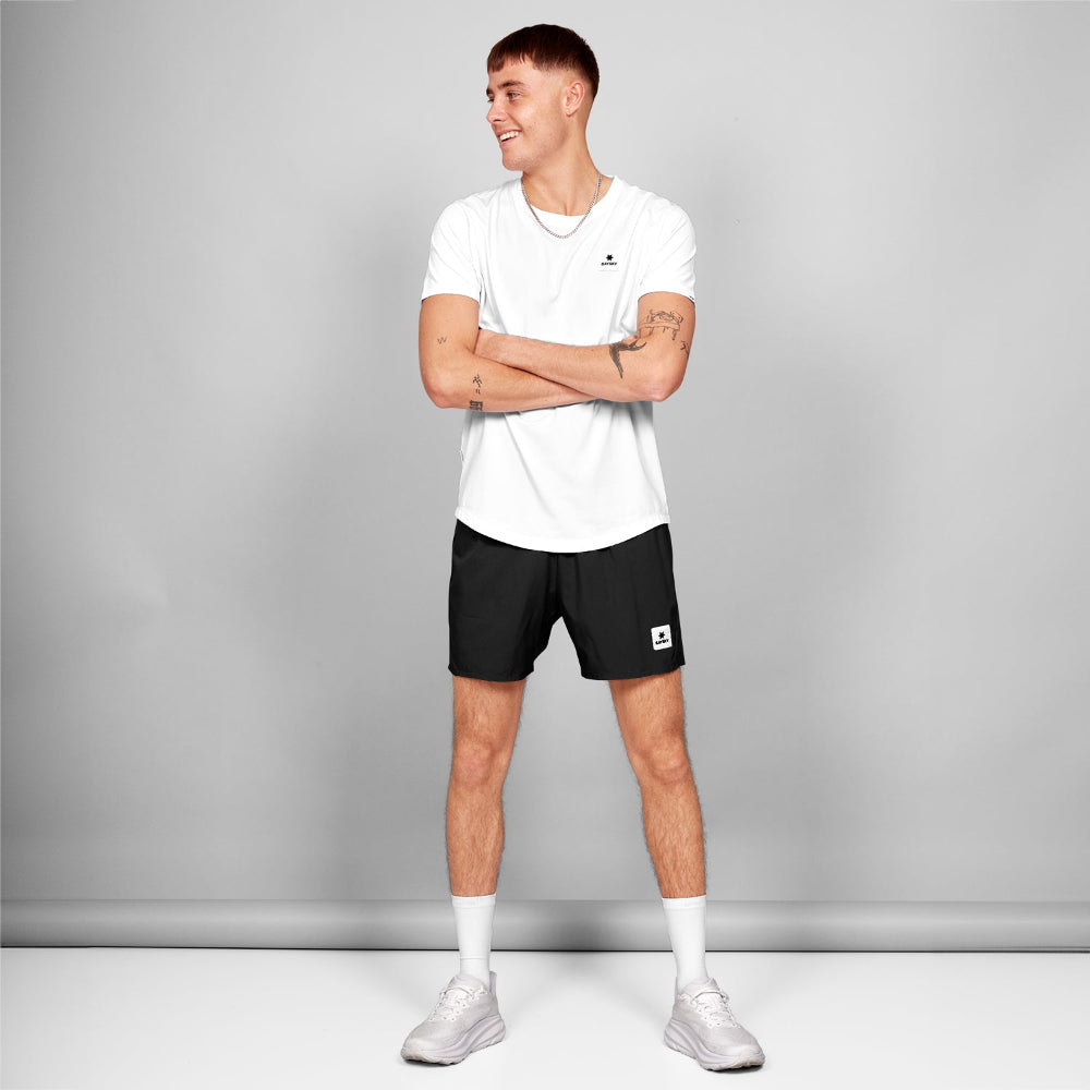 Man wearing a white t-shirt and black shorts with a logo on a gray background