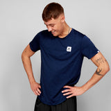 Man wearing a navy blue t-shirt with a small white logo on a gray background