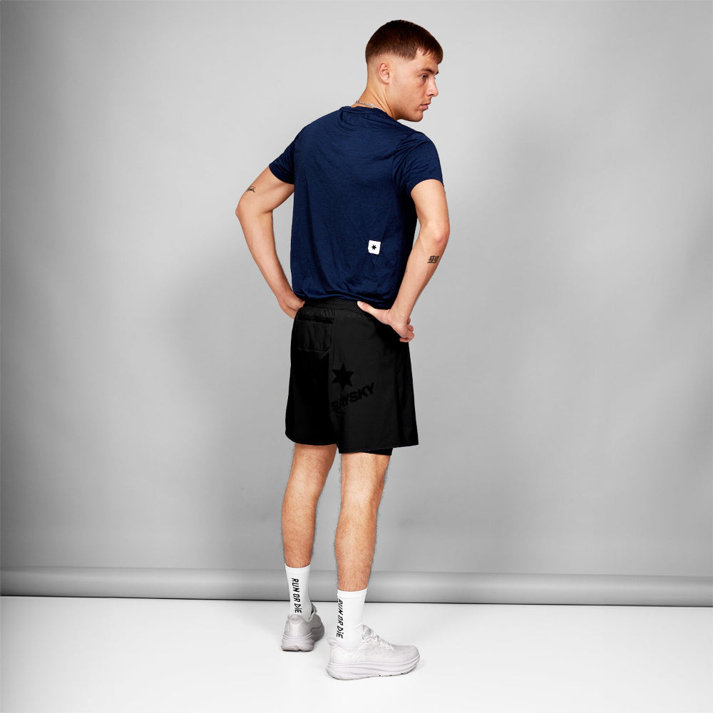 Man wearing a navy t-shirt and black shorts with a logo on a gray background