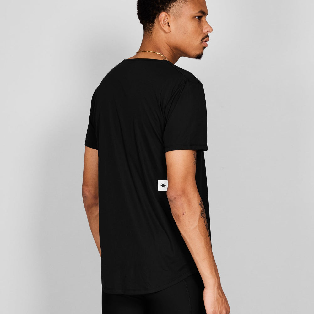 Man wearing a black t-shirt with a small white logo on a gray background