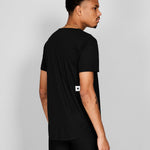 Man wearing a black t-shirt with a small white logo on a gray background
