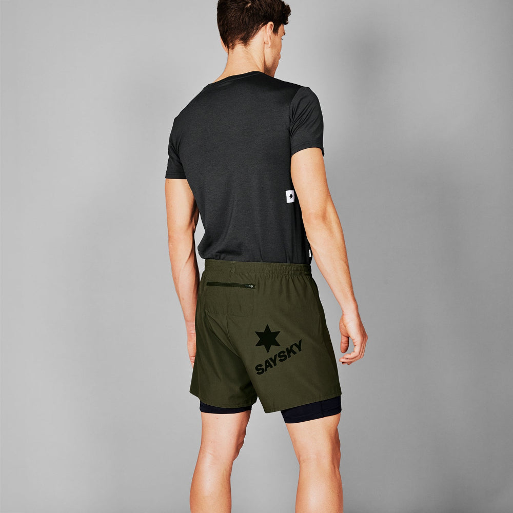 Person wearing a black t-shirt and green shorts with a visible brand logo on a gray background