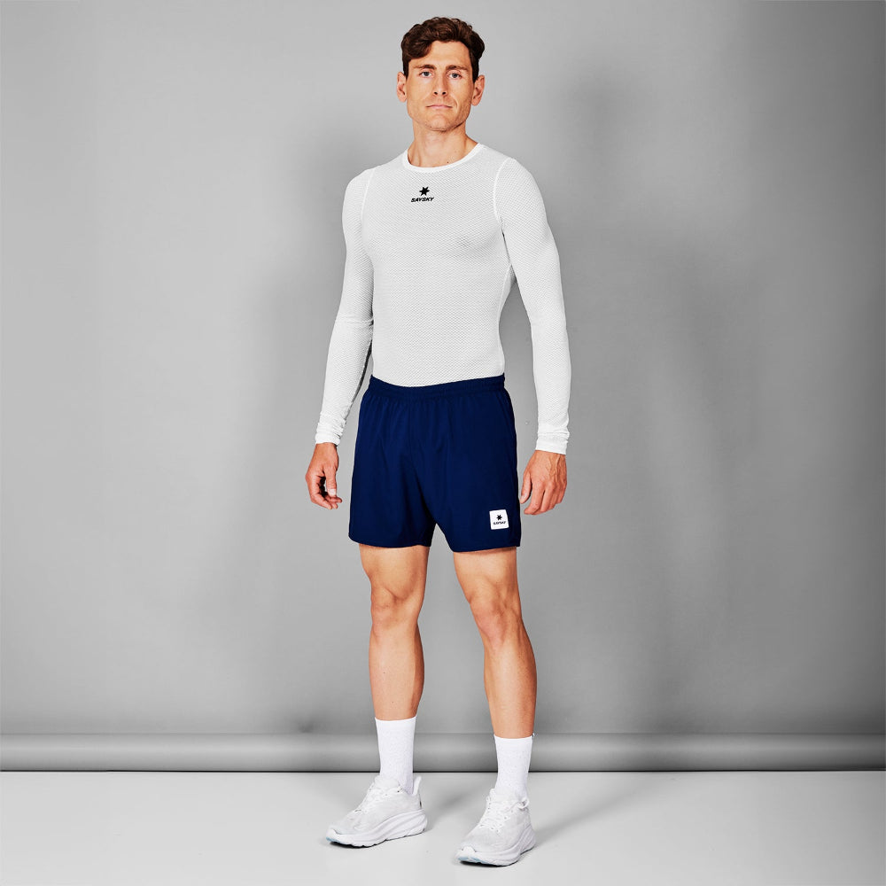 Man wearing a white long-sleeve shirt and navy shorts on a gray background