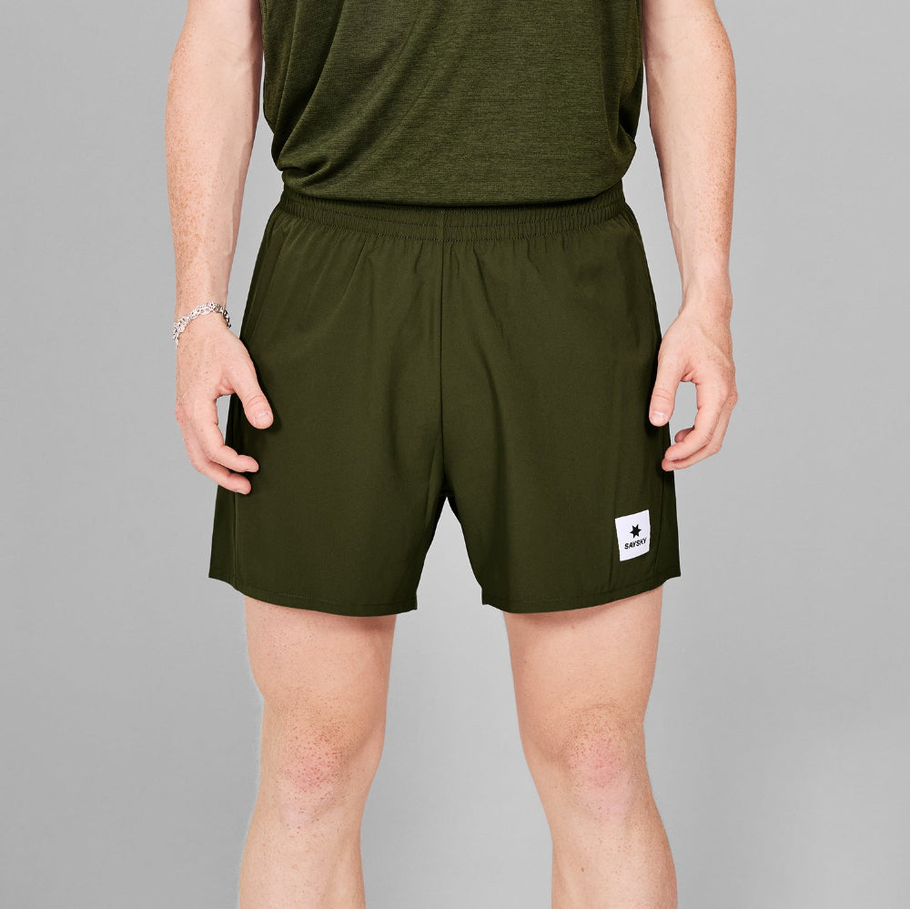 Person wearing green athletic shorts with a small logo on a gray background
