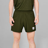 Person wearing green athletic shorts with a small logo on a gray background
