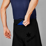 Person wearing black shorts with a star logo and 'Saysky' branding, holding a blue phone.