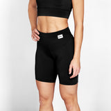Person wearing black athletic shorts with a visible brand logo on a light gray background