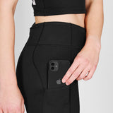 Person wearing black leggings with a phone pocket, holding a black phone.